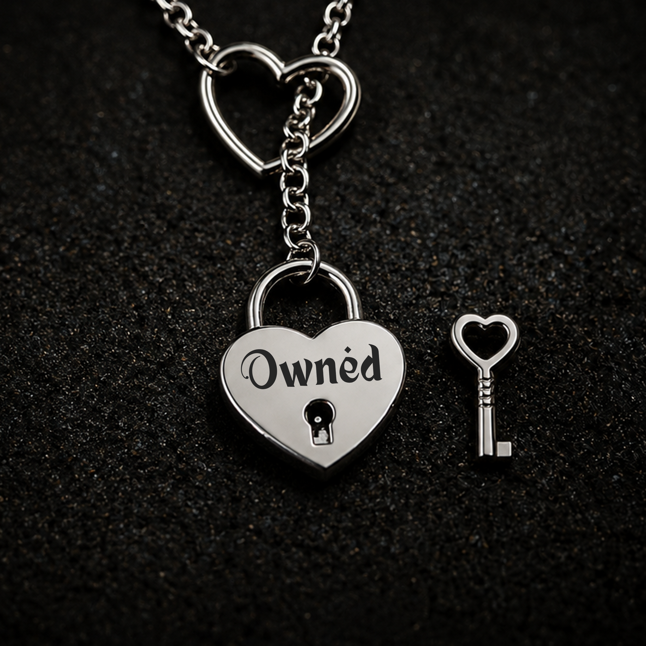 A silver heart-shaped padlock pendant engraved with the word 'Owned' and a small heart-shaped key, displayed on a dark textured background.