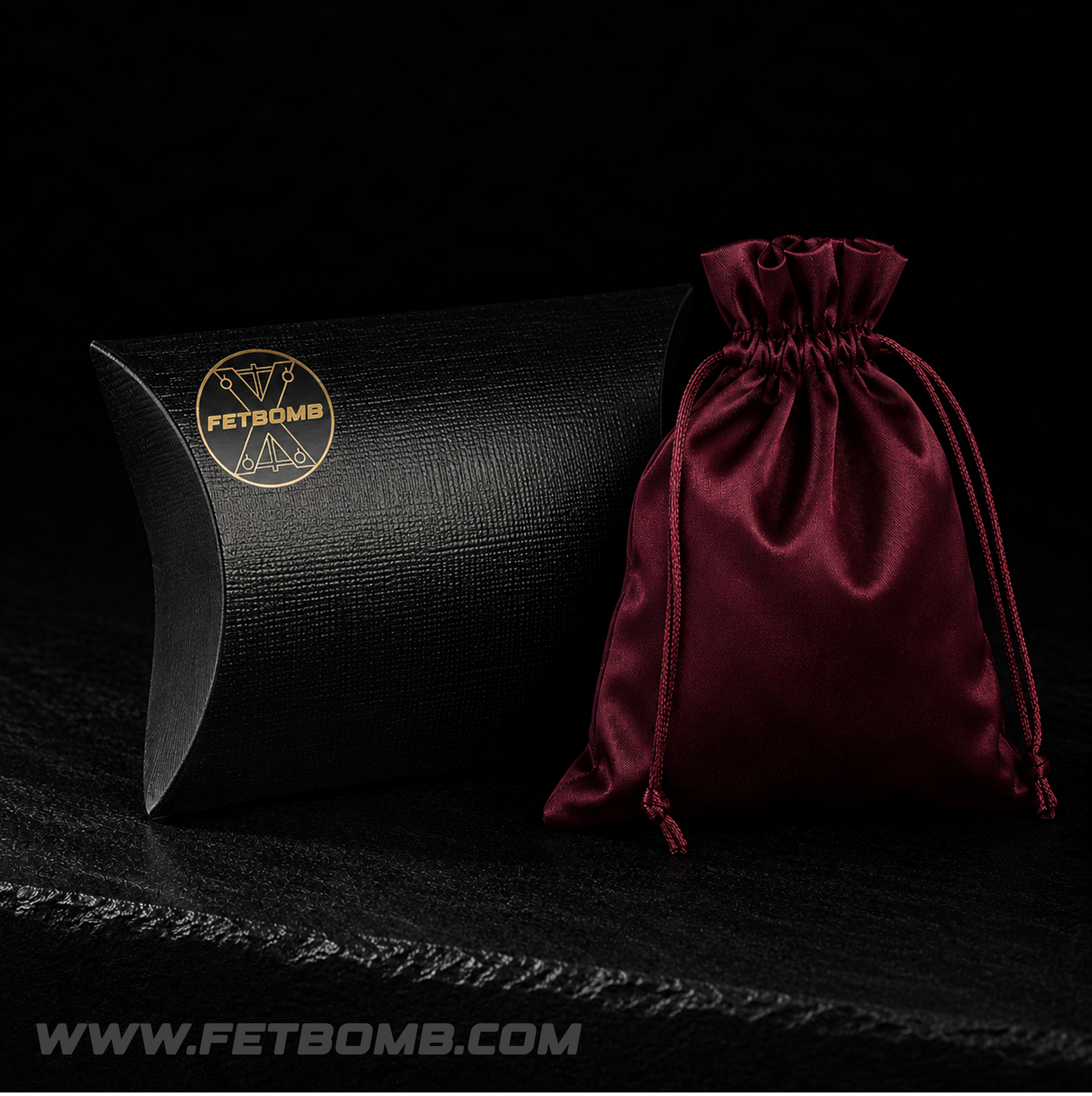 Black pillow-shaped box and red drawstring bag with 'FetBomb' fetish store branding on a dark background.
