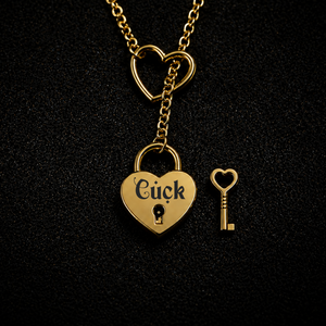 A gold heart-shaped lock pendant necklace with the word 'Cuck' engraved on it, shown with a matching heart-shaped key on a textured black background.