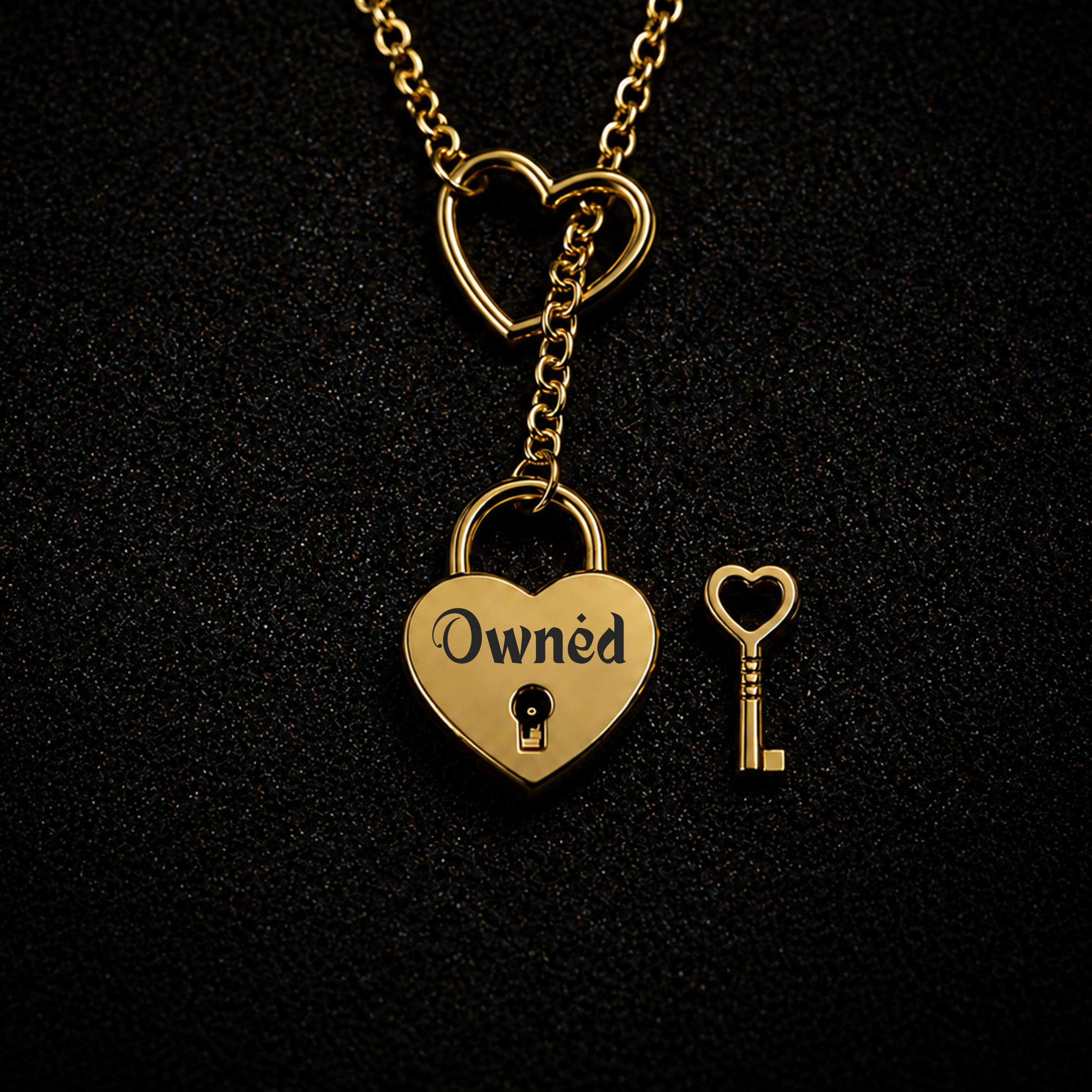 A gold heart-shaped padlock necklace with the word 'Owned' engraved on the padlock body, shown hanging from a heart-link chain next to a small heart-shaped key on a black textured background.