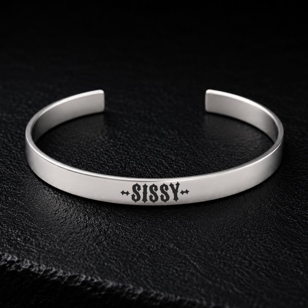 Silver stainless steel cuff bracelet engraved with the word SISSY in bold gothic lettering, photographed on a dark textured background, available from FETBOMB.
