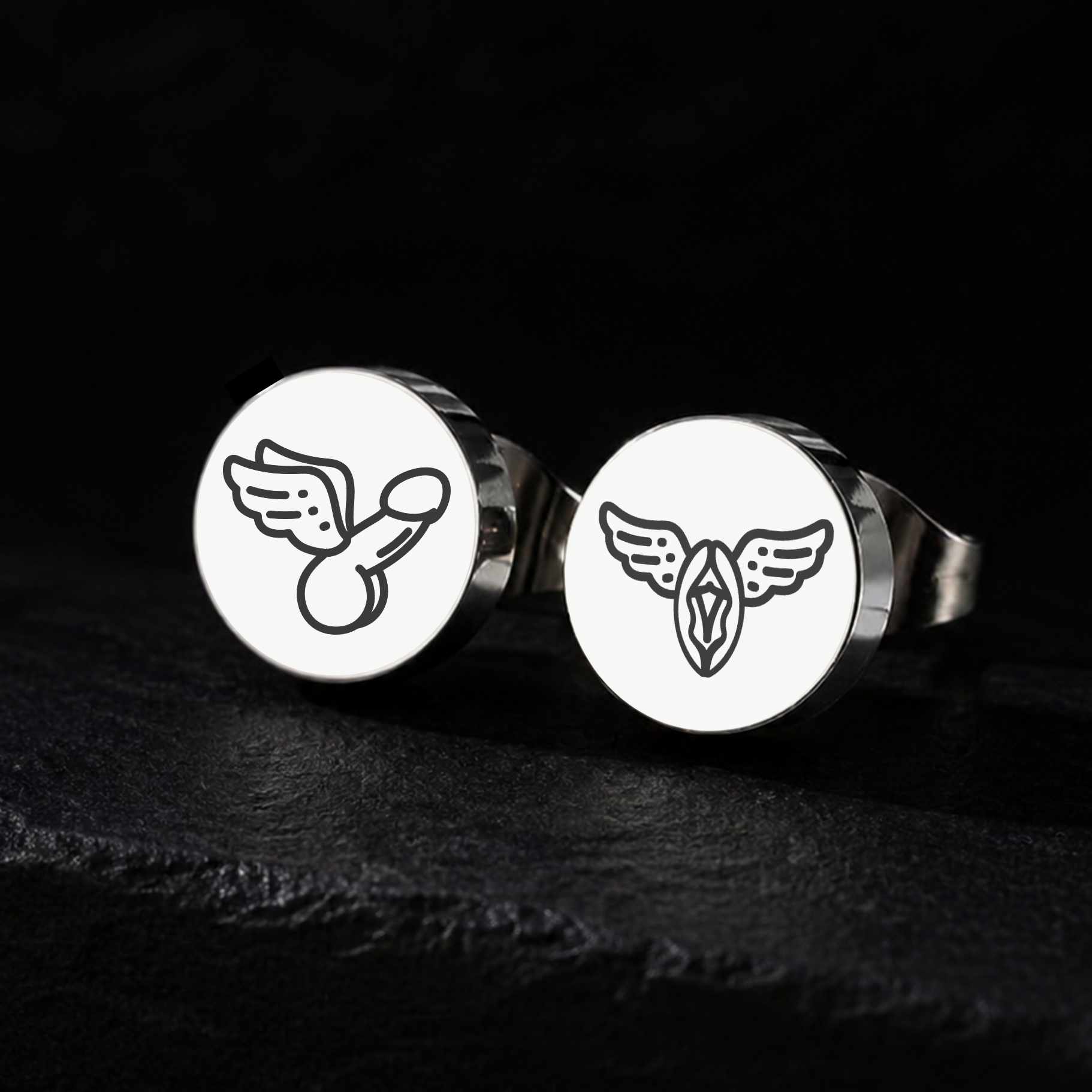 Silver winged penis and winged vagina stud earrings on a black background, explicit fetish jewellery in 12mm stainless steel from FETBOMB.